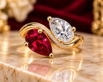 May include: A bypass ring crafted from yellow gold featuring two pear-cut stones, one deep red and one clear white. The band is accented with a row of small pavé-set stones along the curved shank, creating a dual-stone design.