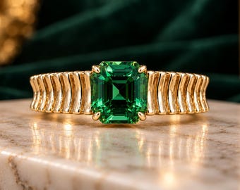 May include: A gold ring featuring a central emerald-cut green gemstone held by four prongs. The band is constructed from a series of vertical, curved gold bars that create a ribbed texture extending around the finger, showcasing a polished finish.