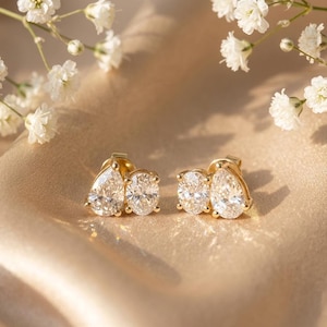 Peut inclure: Une paire de boucles d'oreilles à clous en or, chacune composée d'une pierre précieuse transparente en forme de poire associée à une pierre ovale. Les pierres sont serties dans du métal doré poli, formant un motif groupé brillant.