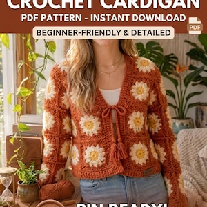May include: A crochet cardigan featuring a pattern of white and yellow daisy motifs on a rust-coloured background. The garment has long sleeves, a V-neckline, and a front tie closure with tassels. Text reads: BOHO DAISY CROCHET CARDIGAN PDF PATTERN.