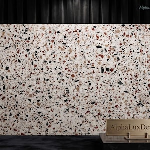 Könnte beinhalten: Eine rechteckige Platte mit einer weißen Terrazzo-Oberfläche, die mit Splittern in Schwarz, Dunkelrot und Hellbraun durchsetzt ist. Im Vordergrund steht ein kleines goldfarbenes Metallschild mit der Aufschrift AlphaLuxDesigns in Schwarz.