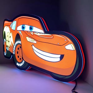 May include: An illuminated wall sign shaped like the character Lightning McQueen from the movie Cars. The sign features a bright orange race car with blue eyes, the number 95, and Lightyear branding on the tires, glowing with internal LED lights.