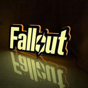 May include: A three-dimensional illuminated sign displaying the word Fallout in a bold, stylized font. The letters feature a bright yellow glow with black outlines and a central lightning bolt symbol replacing the letter O, casting a reflection.