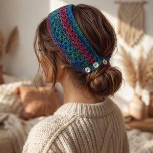 Peut inclure: Un bandeau en crochet arborant un motif multicolore vif composé de fils bleu, vert, violet et magenta. L'accessoire est fixé sur le côté par trois petits boutons ronds blancs, créant une fermeture fonctionnelle pour le tissu tricoté.