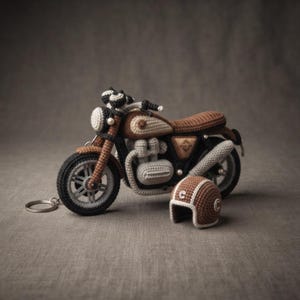 Op de afbeelding: Een gehaakte motorfiets sleutelhanger in bruin en beige met zwarte wielen en een zilveren metalen ring. Een kleine, bijpassende gehaakte helm in bruin en beige met een witte letter C aan de zijkant staat op de grond naast de motorfiets.