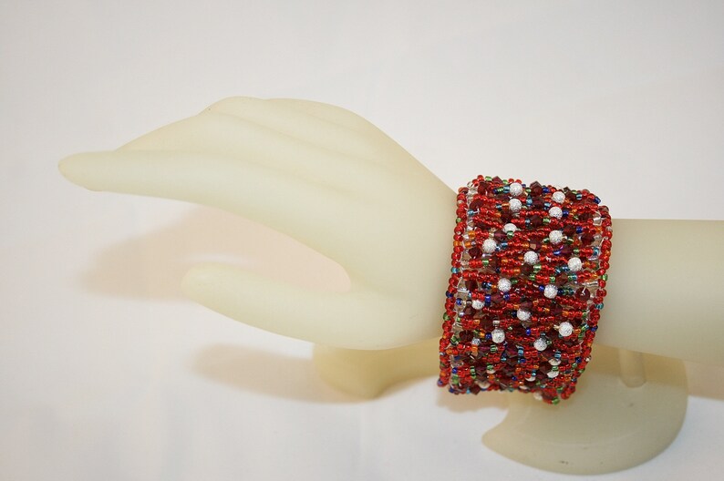 May include: A red, white, and blue beaded bracelet with a geometric pattern. The bracelet is made with small seed beads and larger round beads.