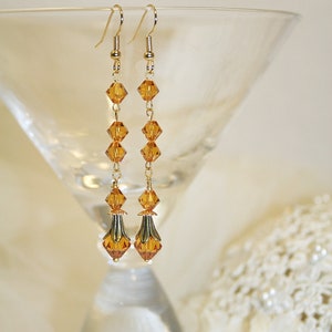 May include: A pair of long gold earrings with amber-colored crystal beads. The earrings have a teardrop shape at the bottom.