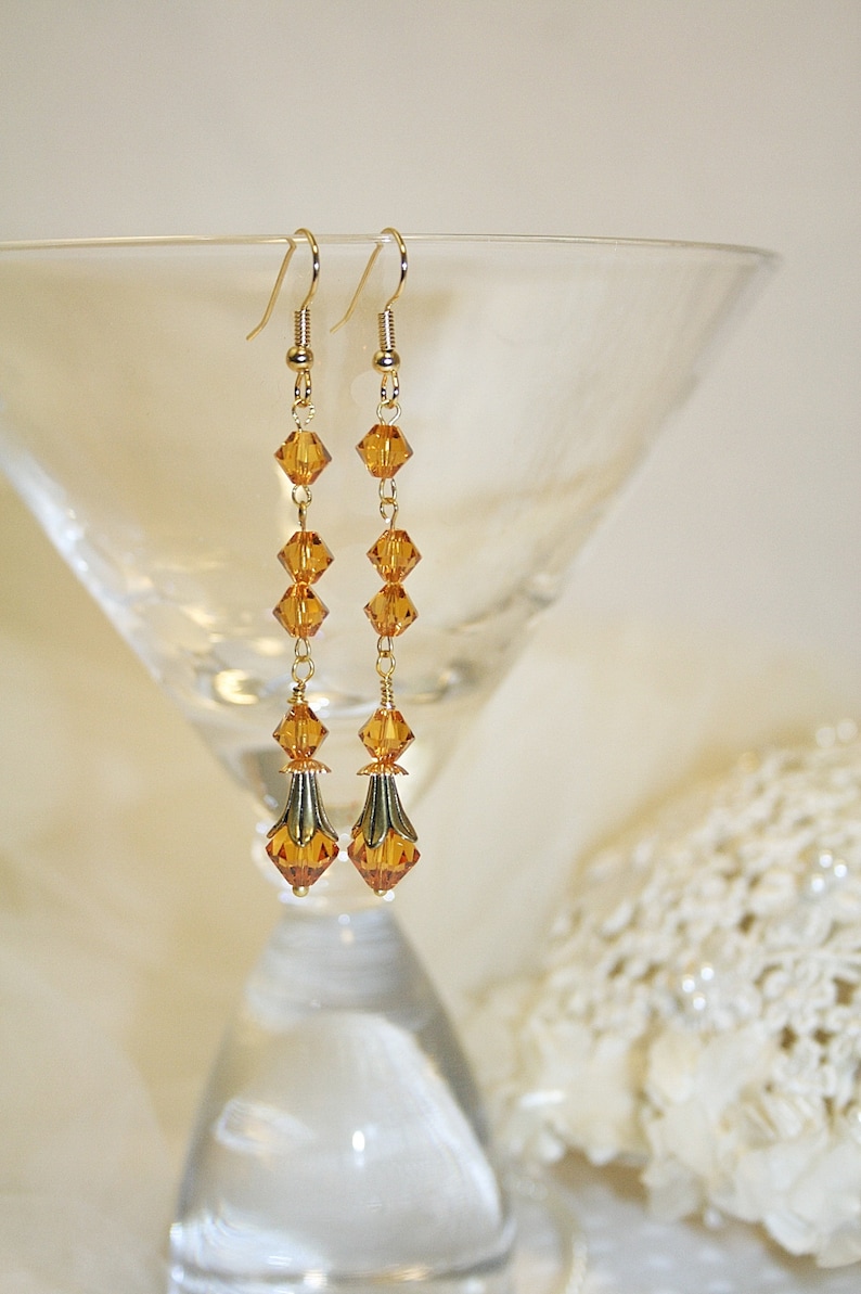May include: A pair of long gold earrings with amber-colored crystal beads. The earrings have a teardrop shape at the bottom.
