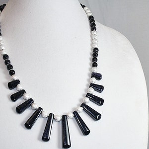 Puede incluir: Un collar de cuentas negras y plateadas con un colgante de formas de l&aacute;grima de piedra preciosa negra.