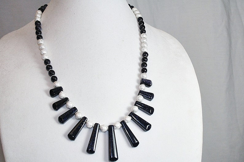 Puede incluir: Un collar de cuentas negras y plateadas con un colgante de formas de l&aacute;grima de piedra preciosa negra.