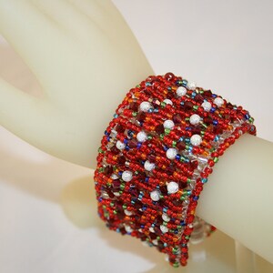May include: A red, white, and blue beaded bracelet with a multi-colored design. The bracelet is made with small, round beads and is woven in a complex pattern.