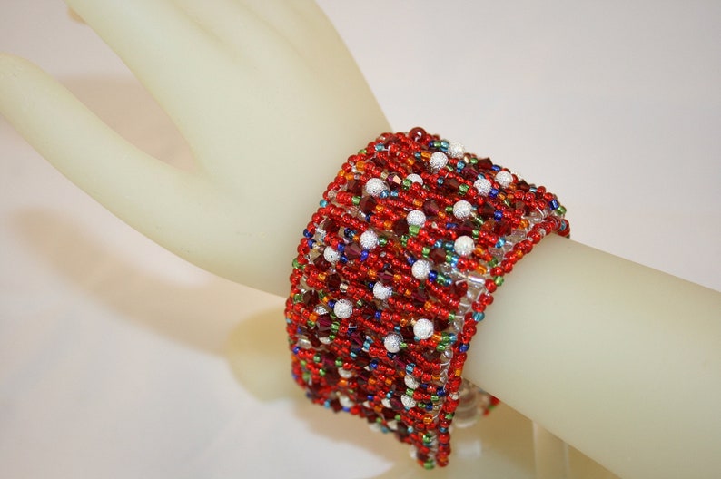 May include: A red, white, and blue beaded bracelet with a multi-colored design. The bracelet is made with small, round beads and is woven in a complex pattern.