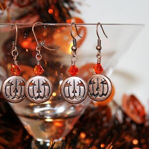 Puede incluir: Pendientes de calabaza de cobre con detalles de cristal naranja. Los pendientes cuelgan de una copa de martini de vidrio.