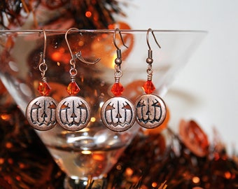 May include: Copper pumpkin earrings with orange crystal accents. The earrings are hanging from a glass martini glass.