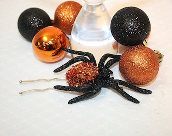 May include: A black spider with a brown and orange pom-pom on its back, surrounded by black and orange glitter ornaments.