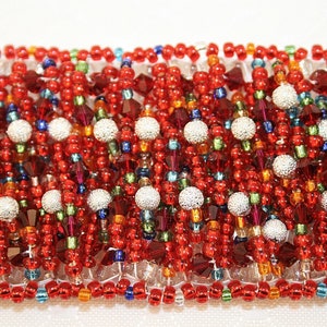 May include: A close-up of a beaded bracelet with a red, orange, green, blue, and silver color scheme. The bracelet is made of small, round beads and has a textured, woven appearance.
