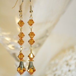 May include: A pair of long gold dangle earrings with amber-colored crystal beads. The earrings have a teardrop-shaped crystal at the bottom.
