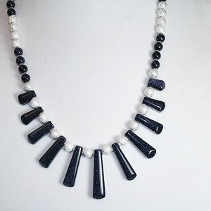 Puede incluir: Un collar de cuentas negras y plateadas con una fila graduada de piedras de color azul oscuro, facetadas, en forma de l&aacute;grima.
