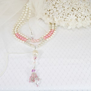 Puede incluir: Un collar de perlas de varias hebras con cuentas rosadas y blancas y un colgante de cristal y perlas.