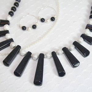 Puede incluir: Un collar negro y plateado con un colgante hecho de varias piezas de piedras preciosas azules. El collar se combina con pendientes a juego.