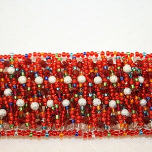 May include: A red, white, and blue beaded bracelet with silver accents. The bracelet is made of small, round beads and is woven in a complex pattern.