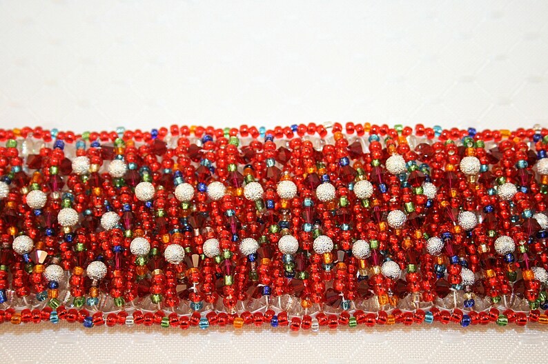 May include: A red, white, and blue beaded bracelet with silver accents. The bracelet is made of small, round beads and is woven in a complex pattern.
