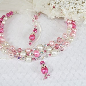 Puede incluir: Un collar de múltiples hilos con cuentas rosas, blancas y transparentes. El collar tiene un colgante de lágrima rosa.