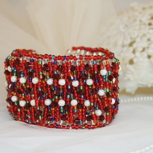 May include: A red, white, and blue beaded bracelet with a geometric pattern. The bracelet is made with small glass beads and has a shiny finish.