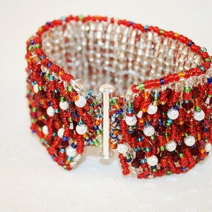 May include: A red, white, and silver beaded bracelet with a silver clasp. The bracelet is made of small, round beads and has a textured, woven design.