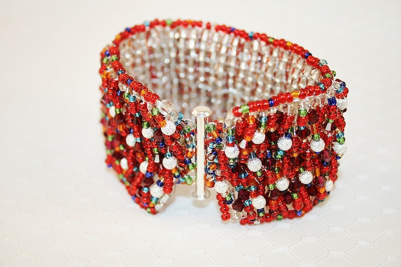 May include: A red, white, and silver beaded bracelet with a silver clasp. The bracelet is made of small, round beads and has a textured, woven design.