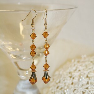May include: A pair of long, gold dangle earrings with amber-colored crystal beads. The earrings have a teardrop-shaped crystal at the bottom.