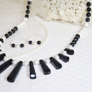 Puede incluir: Un collar negro y plateado con un colgante hecho de varias piedras negras. El collar se combina con pendientes de aro a juego.