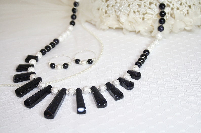 Puede incluir: Un collar negro y plateado con un colgante hecho de varias piedras negras. El collar se combina con pendientes de aro a juego.