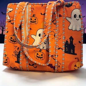 May include: A quilted tote bag in bright orange featuring a repeating Halloween pattern of white ghosts, black jack-o'-lanterns, dark silhouettes of haunted houses, bats, and spiders. The bag has two matching fabric handles with striped edges.