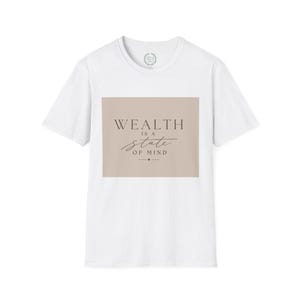Può includere: Una t-shirt bianca a maniche corte con una grafica rettangolare color beige sul petto. La grafica contiene il testo marrone scuro "WEALTH IS A state OF MIND" in una combinazione di caratteri serif e corsivi, con un piccolo simbolo a rombo sotto.