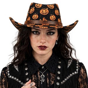 Könnte beinhalten: Ein Cowboyhut mit schwarzer Grundfarbe und einem durchgehenden orangefarbenen Kürbis-Print. Der Hut verfügt über ein braunes Band um die Krone, eine strukturierte Krempe und ein eingekniffenes Oberteil mit einem markanten saisonalen Muster.