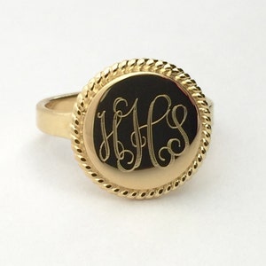 May include: A gold ring with a round face featuring a rope-like border and engraved initials "HHS".