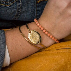May include: A woman wearing a denim jacket and a yellow leather handbag with a tassel. She is wearing a gold bracelet with a round charm and a coral beaded bracelet.
