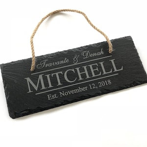 May include: Black slate sign with a rope hanger. The sign is engraved with the text "Travante & Denah Mitchell Est. November 12, 2018".
