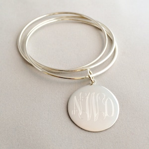 May include: A silver bangle bracelet set with three bands and a round charm with an engraved monogram.