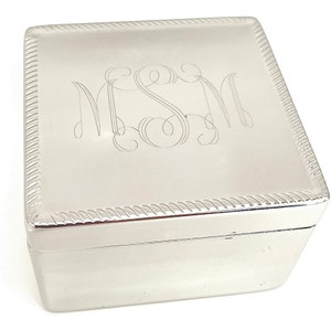 May include: A silver square box with a rope-like border around the edge. The top of the box has the monogram "MSM" engraved in a script font.