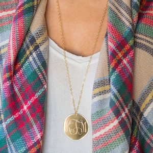 May include: A gold chain necklace with a large round pendant featuring a monogram. The pendant is engraved with the letters "KSM". The necklace is worn by a person wearing a plaid scarf.