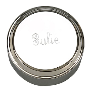 May include: A silver round trinket box with a raised rim and the name "Julie" engraved on the lid.