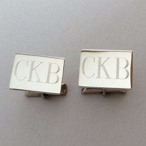 May include: A pair of silver cufflinks with the initials "CKB" engraved on each.