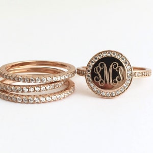 Puede incluir: Un conjunto de anillos de oro rosa con una pieza central circular grabada con las letras SMS en letra cursiva. La cara circular y las bandas de los anillos est&aacute;n incrustadas con peque&ntilde;as piedras redondas y transparentes que reflejan la luz.