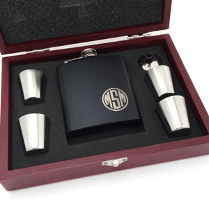 May include: A black flask with a monogrammed circle reading "MSM" in silver lettering, in a wooden box with two shot glasses and a funnel.