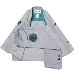 May include: A light gray Brazilian Jiu-Jitsu gi set consisting of a jacket and pants. The jacket features teal interior lining, black logos, and geometric stitching. The pants include a drawstring waist and a circular patch with black text.