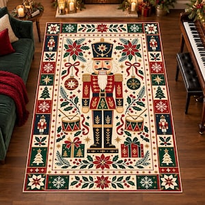 Op de afbeelding: Een rechthoekig vloerkleed met een centrale notenkrakerfiguur in een rood, blauw en goud uniform. Het ontwerp bevat kerststerren, dennentakken, trommels, cadeaus en sneeuwvlokken in een feestelijk kleurenpalet van rood, groen en crème.