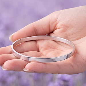 Peut inclure: Un bracelet jonc en argent poli avec une surface lisse et plate de forme circulaire. La bande métallique présente un petit poinçon clair indiquant 925 sur le côté intérieur, ce qui confirme la composition en argent sterling de ce bijou.