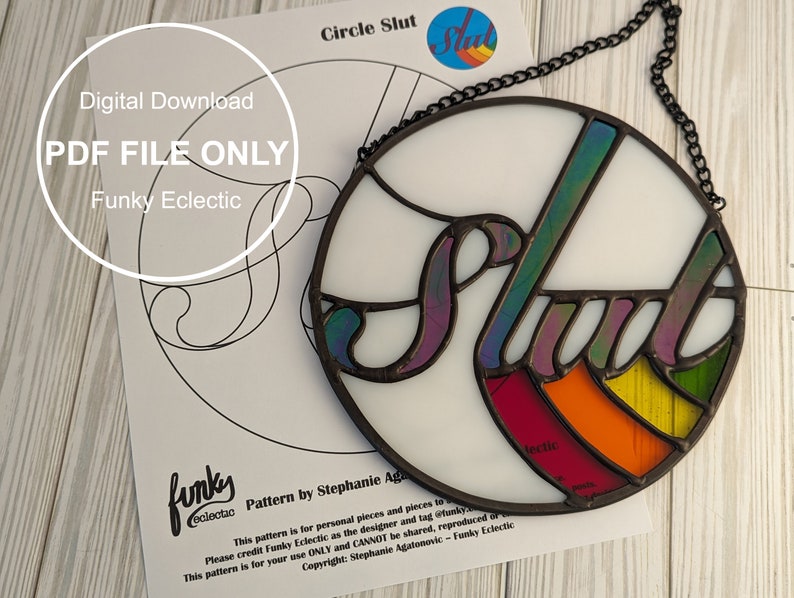 May include: A stained glass window hanging with a chain. The glass is white with a rainbow colored design and the word "Slut" in a stylized font.